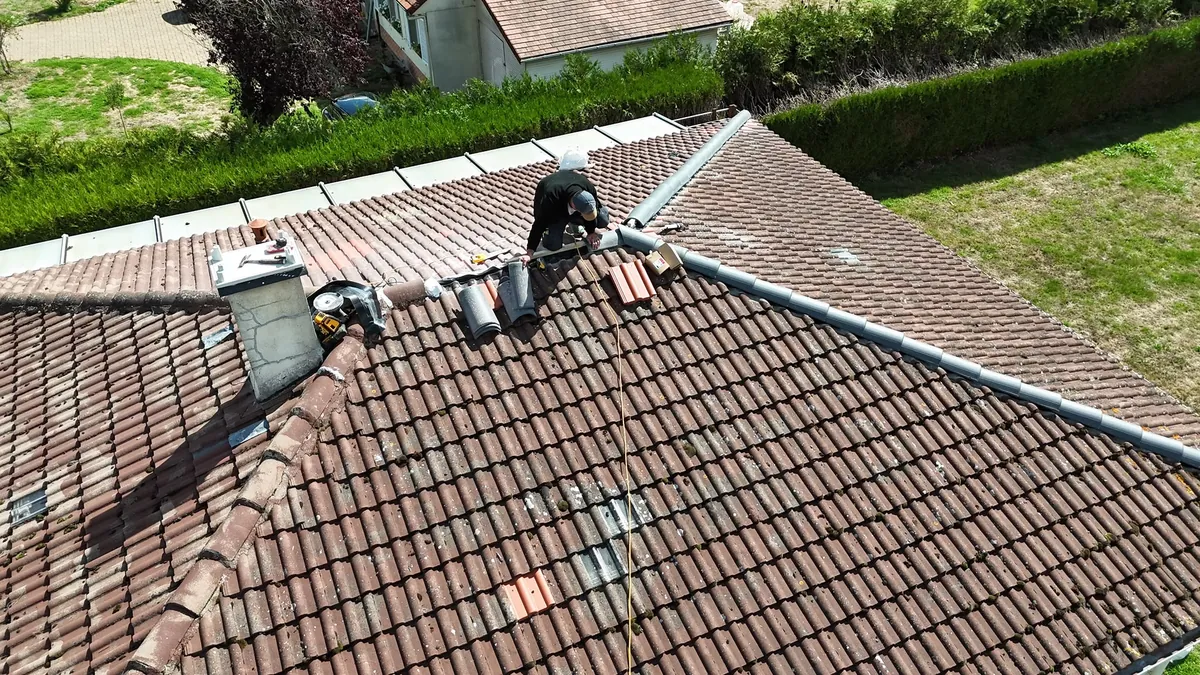Couvreur au travail sur une toiture en tuile plate, faîtage en cours de reprise