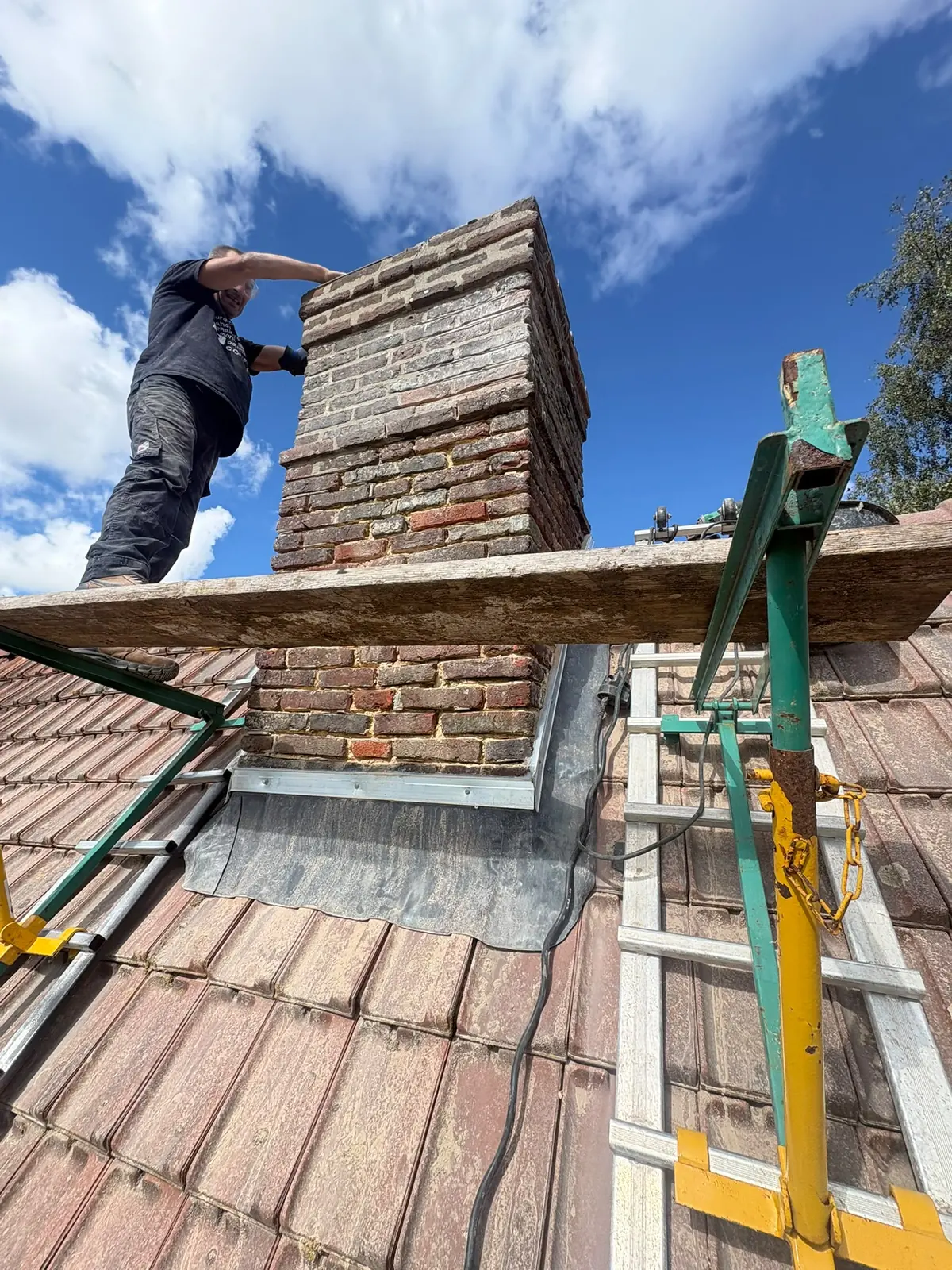 Couvreur au travail au pied d’une souche de cheminée en brique, sur une toiture en tuile